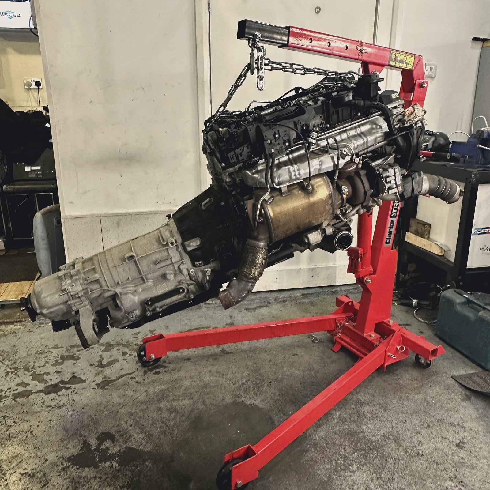 A complete engine and gearbox assembly hanging from an engine crane
