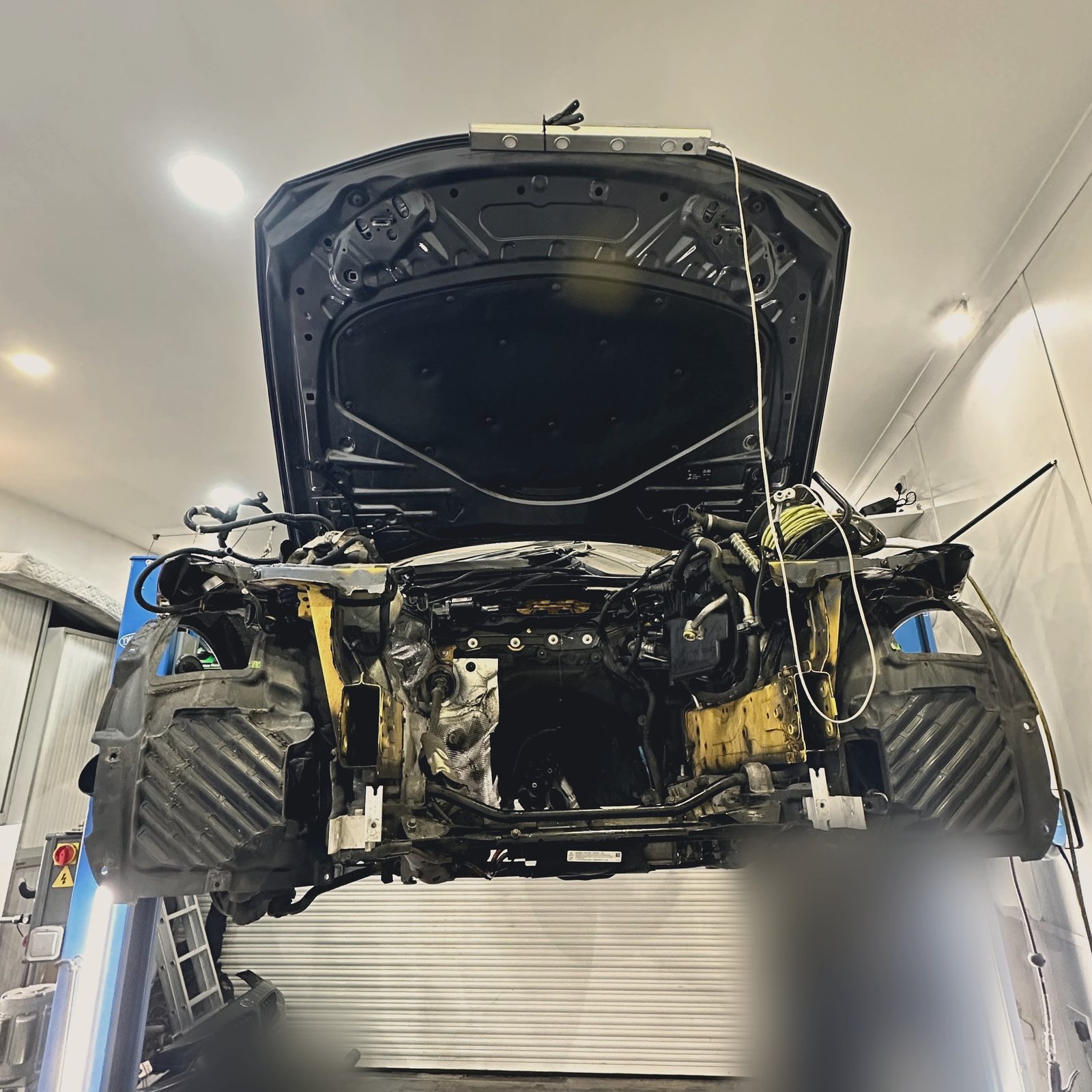 A car on a two-post lift with the hood open, viewed from below